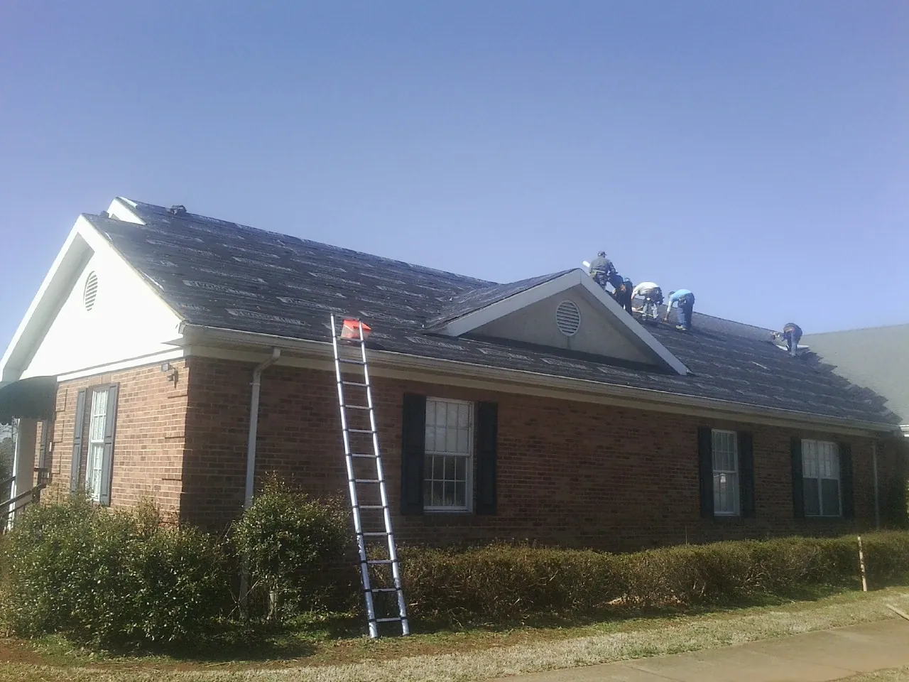 Crew tearing shingles off a brick ranch roof with a ladder set — Metal Roof Repair work by our crew in Ransom