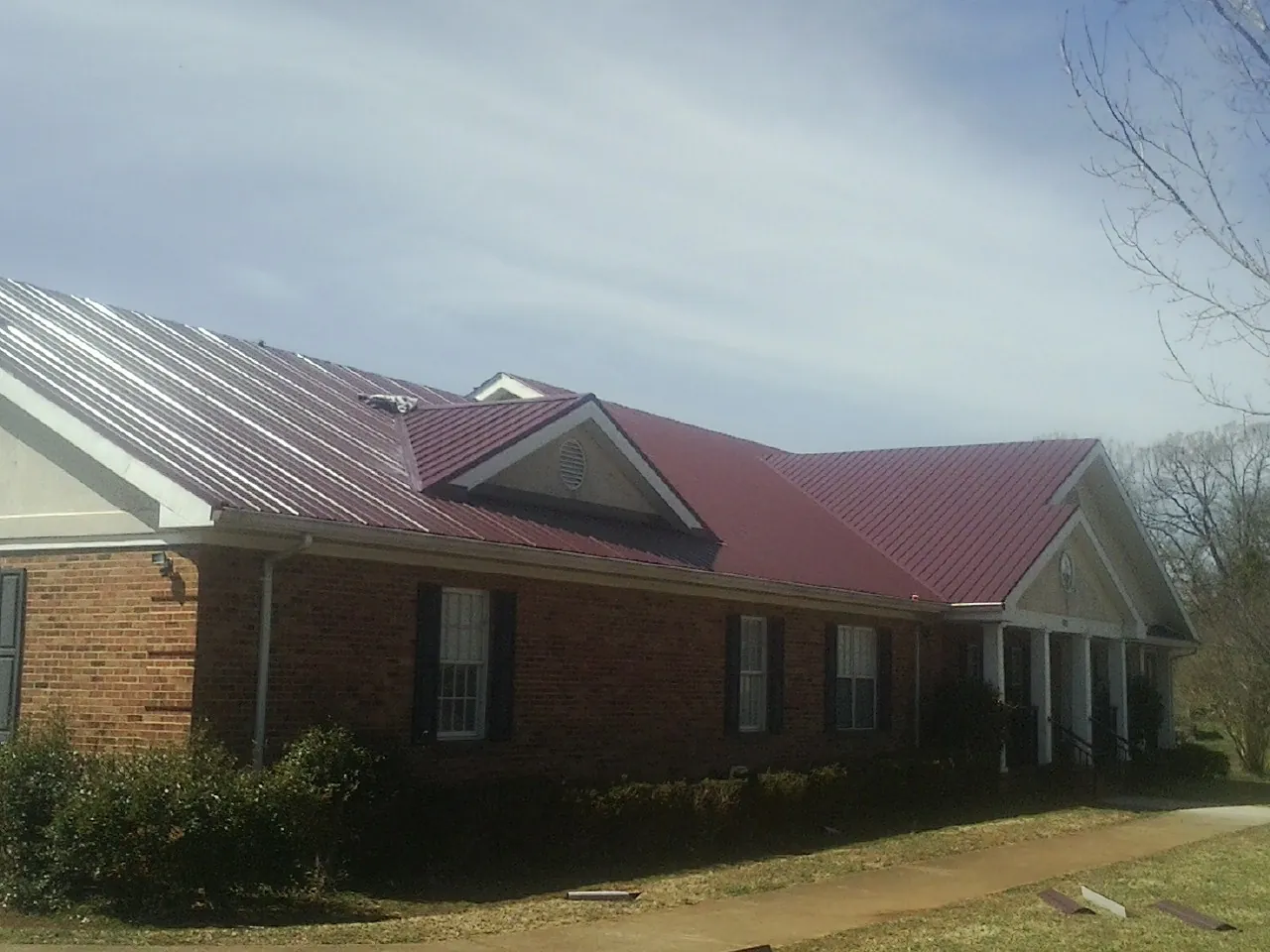 Red metal roof with gabled entries on a long brick building, from a Hail Damage Roof Repair job in Ransom