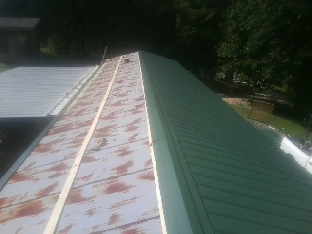 Old rusted panels beside newly installed green metal roofing — Wind Damage Roof Repair by Roofing Brothers in Ransom