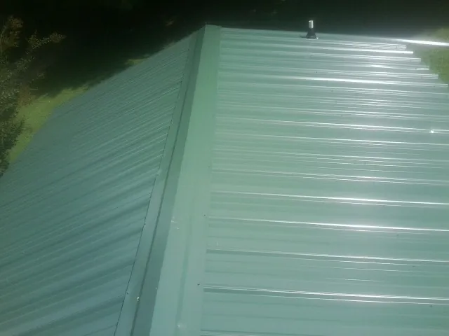 New green metal panels meeting at the ridge of a roof — Flat Roof Repair work by our crew in Ransom