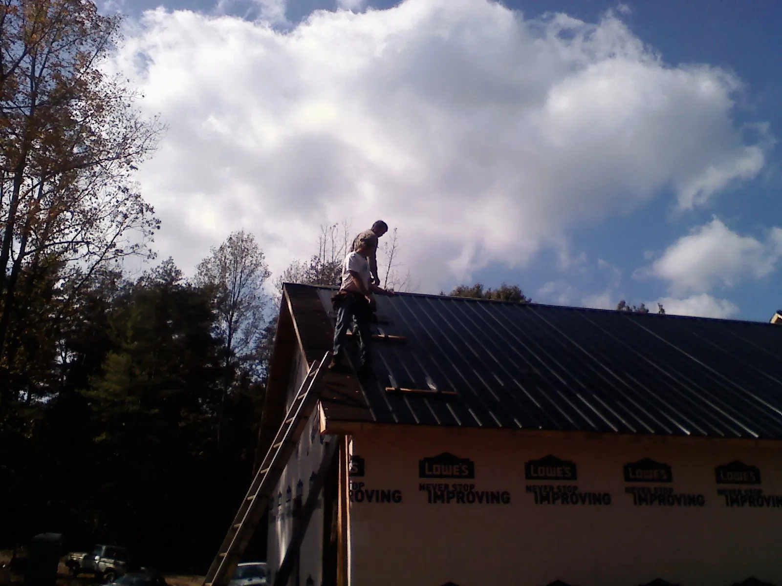 Roofer fastening dark metal panels high against a cloudy sky, from a Roof Inspection job in Ransom